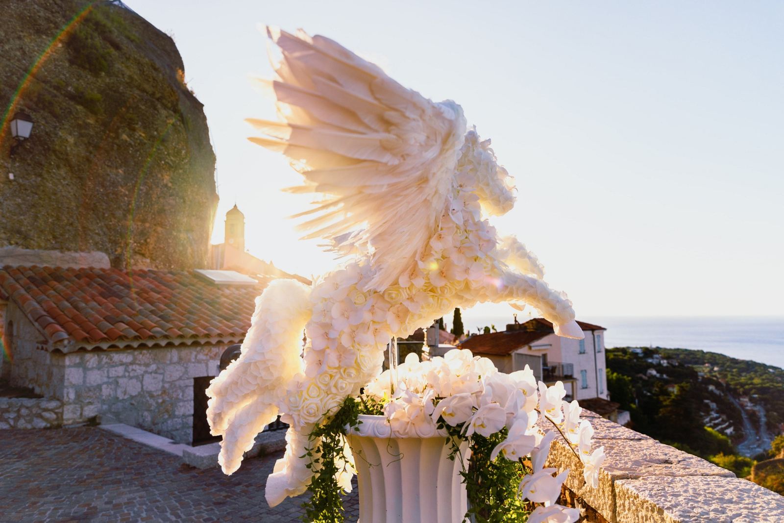 A life size Pegasus sculpted in white flowers and feathers, backlit by the sun