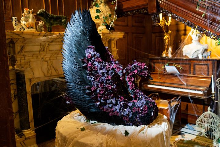 The black swan sculpture in a wood panelled room beside a piano