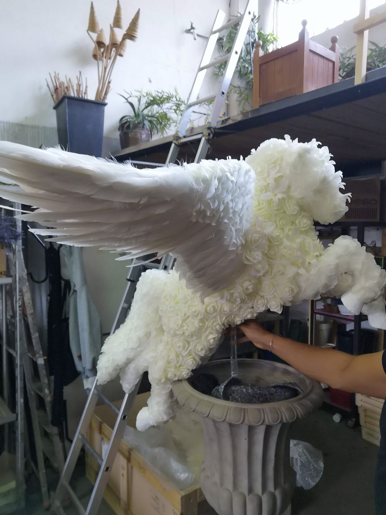 Hands setting white blooms into the body of the Pegasus in the atelier